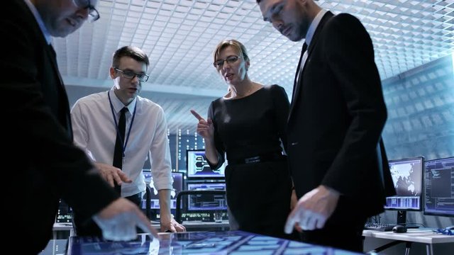Team of Government Agents Tracking Fugitive with Help of Touchscreen Interactive Table in State of the Art Monitoring Room Full of Computers with Animated Screens. 