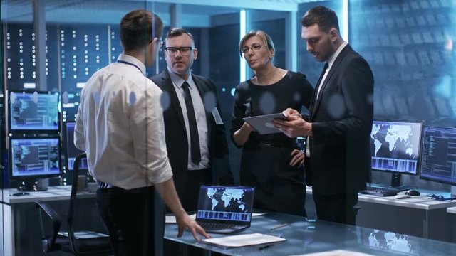 Team of Corporate Managers Working at the Table in Monitoring Room.  They're in State of the Art Facility. Computers have Animated Screens. Shot on RED EPIC-W 8K Helium Cinema Camera.