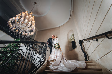 The bride and groom are standing on the stairs with forged rails.