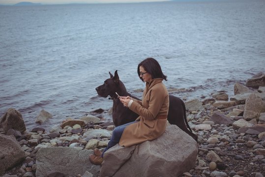 Woman using mobile phone by dog at beach