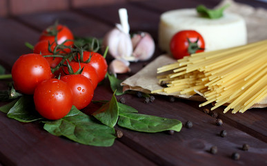 Cherry tomatoes, spaghetti, basil, garlic, cheese on the dark wood background
