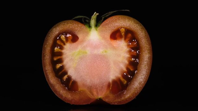 Close up of slit pink tomato with stem, rotating on black background to the right, contra-clockwise. Amazing texture of fresh vegetable in 4k, 3840x2160, clip.
