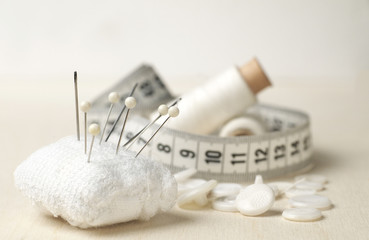 Sewing accessories: pin cushion, buttons, threads, measuring tape, thread bobbins, Shallow depth of field.