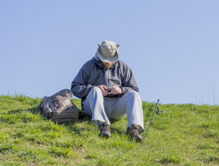 Naklejka na ściany i meble Man sitting on grassy bank cutting fishing line and preparing his gear to catch fish