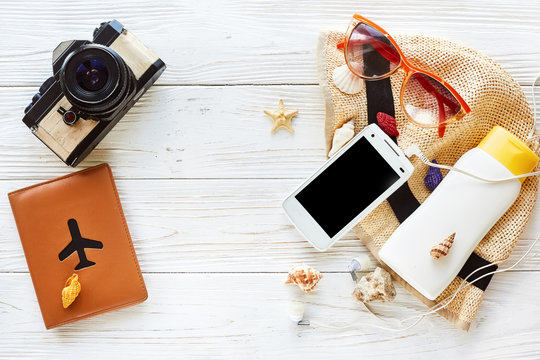 summer travel vacation flat lay concept. photo camera and passport plane hat  phone with empty screen and sunglasses on white wooden background, top view. hello summer. space for text