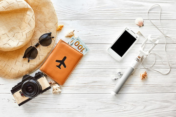 summer travel vacation concept flat lay, space for text. selfie stick phone camera passport money plane hat and sunglasses and shells on white wooden background top view. hello summer.