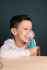 Beautiful sick boy inhalation therapy by the mask of inhaler. Image of a cute kid with respiratory problem or asthma. View of nebulizer with smoke from oxygen mask.