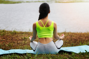 Young asian woman in sportswear meditating on yoga mat, back view