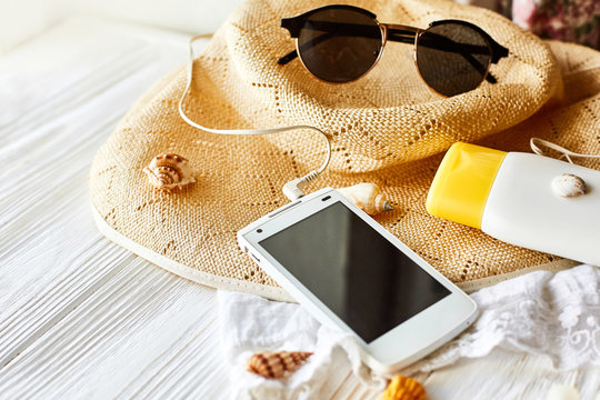 summer travel vacation concept, space for text. phone with empty screen and sunglasses and sunscreen shells hat on white wooden background. hello summer. wanderlust