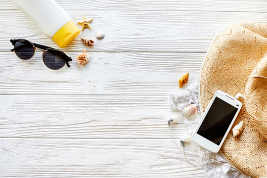summer travel vacation concept, flat lay, space for text. phone with empty screen and sunglasses and sunscreen shells hat on white wooden background top view. hello summer. wanderlust