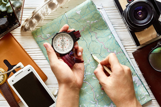 wanderlust and travel concept flat lay. hand holding compass and pencil on map exploring. passport money glasses photo camera  phone on white wooden background. planning vacation. space for text