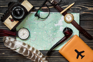 time to travel concept, hipster flat lay. map passport compass and glasses pipe camera  feathers on black  wooden background top view. planning vacation. space for text, wanderlust and explore