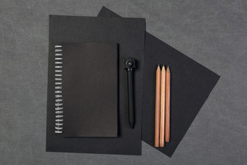 Top view of closed black cover notebook with pencil and pen on gray background