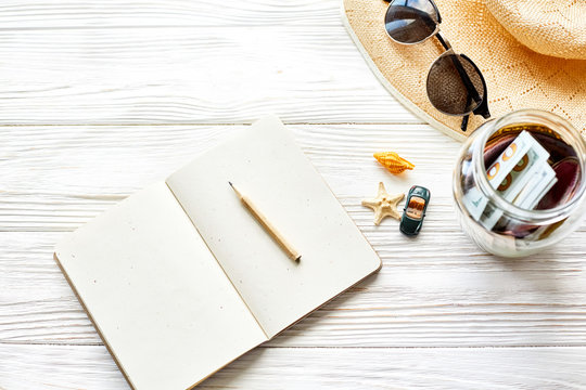 planning summer travel concept and wanderlust, space for text. empty notebook with pen money jar sunglasses hat shells car toy on white wooden background. hello holiday vacation.