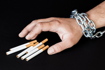 Cigarettes and hand of a man tangled in chains . The concept of nicotine addiction.