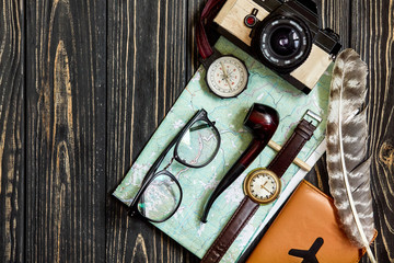 Fototapeta na wymiar wanderlust and travel concept, hipster flat lay. map passport compass and glasses photo camera pipe on black wooden background top view. planning vacation. space for text