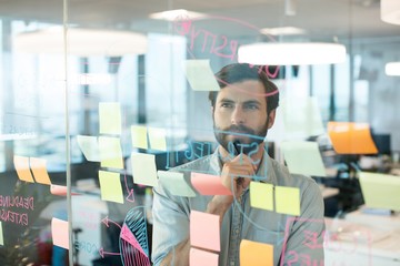 Thoughtful businessman looking at strategy written on glass - obrazy, fototapety, plakaty
