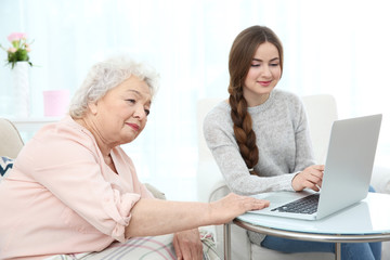 Beautiful girl with grandmother using laptop at home