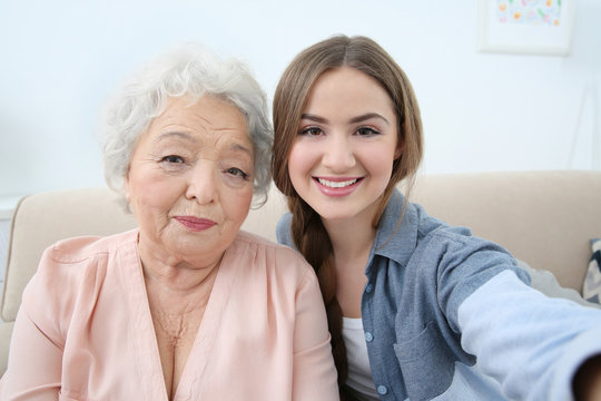 Beautiful girl with grandmother taking selfie on couch at home