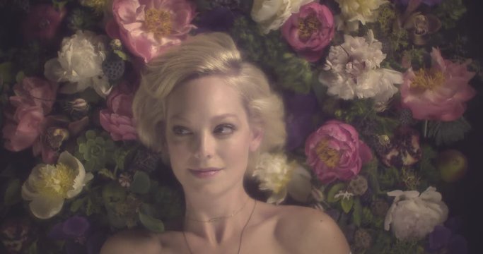 Beautiful blonde woman lies in bed of flowers