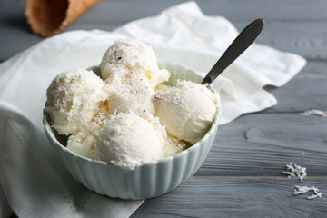 Bowl with balls of ice cream and desiccated coconut on grey wooden table