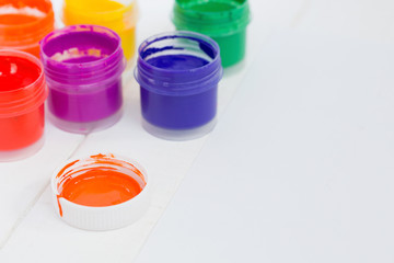 Open jars with colorful paint on a white wooden background