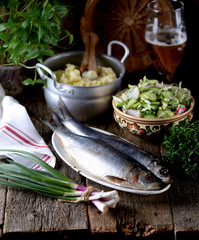Salted herring with mashed potatoes and cucumber salad, radish and cabbage with olive oil on an old wooden background. Rustic style.