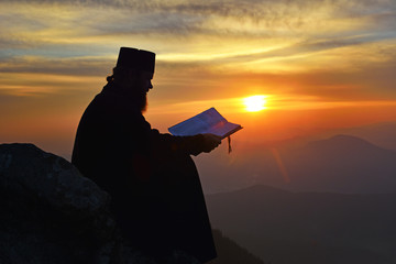 silhouette of priest reading in the sunset light, Romania
