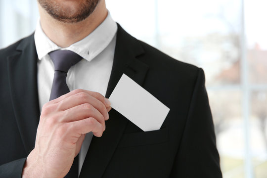 Handsome young man with business card on blurred background, closeup