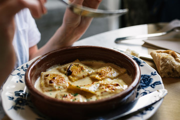 Person eating raviolis with gratin cheese, in restaurant