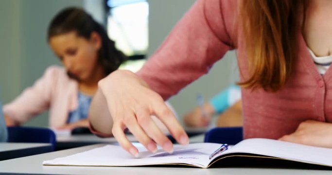 Schoolgirl passing chit to her classmate during exam in classroom