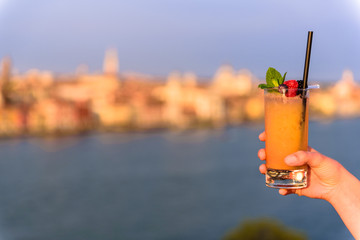 Yellow cocktail in the hand of a girl on the terrace of a building. In the background the city of Venice