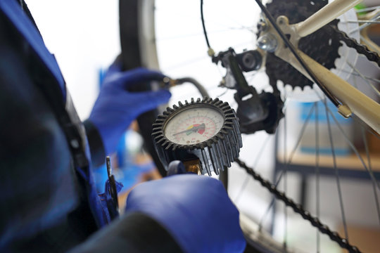 Pompowanie koła rowerowego. Mechanik w serwisie rowerowym pompuje koło roweru kompresorem ze sprężonym powietrzem.