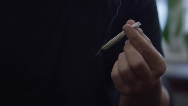 A man smoking a marijuana weed joint in slow motion inhaling smoke