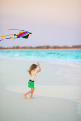 Little girl with flying kite on tropical beach. Kid play on ocean shore. Child with beach toys.