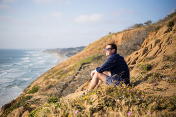 Naklejka na ściany i meble Young man, boy sitting on the cliff in San Diego, California. Sunset cliff. Meditation