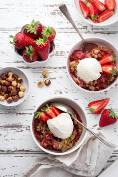 Homemade strawberry and rhubarb crumble with vanilla ice-cream served with fresh berries on light wooden background; Overhead shot