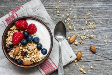 bowl of oat granola with yogurt, fresh raspberries, blueberries and nuts