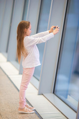 Fototapeta na wymiar Little girl in airport near big window while wait for boarding