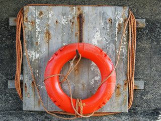 life buoy on a weathered wooden board with faded orange rope in a harbour
