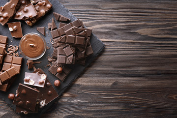 Slate plate with melted chocolate and chopped bars on wooden background
