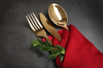 Table setting with golden cutlery in red napkin on grunge background