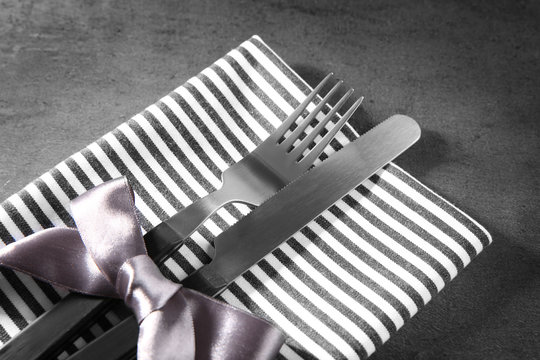Table setting with silver cutlery in striped napkin on grunge background