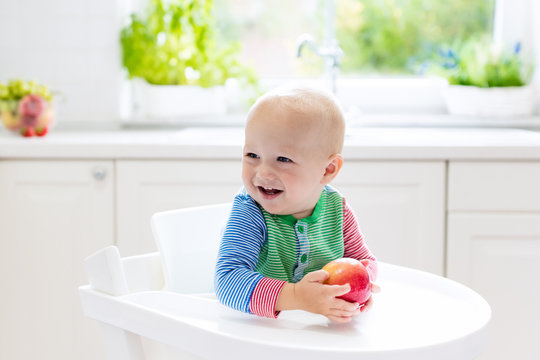Baby boy eating apple in white kitchen at home