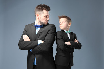 Father and son dressed in suits on color background