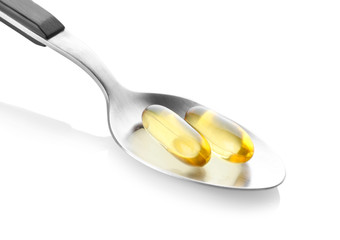 Spoon with fish oil capsules on white background