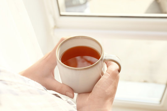 Woman with cup of hot tea near window, closeup
