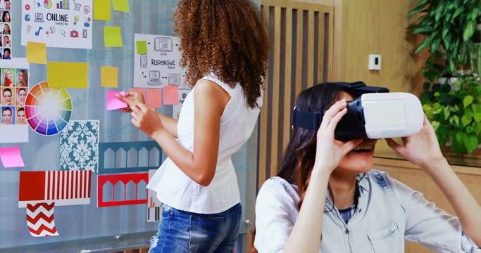 Female executive using virtual reality headset and colleague looking at sticky notes