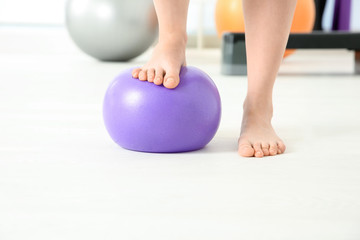 Fototapeta na wymiar Feet of woman doing exercises with rubber ball in clinic