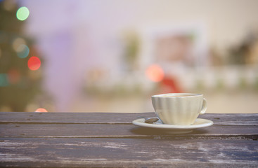 a cup of hot coffee on wooden table with a blurry Christmas trees and lights background, filtered tones